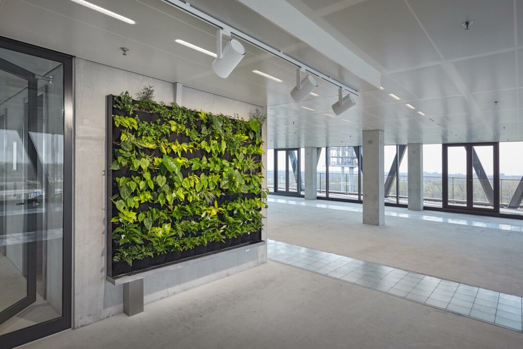 Lichte, moderne kantoorruimte aan de Joan Muyskenweg met een groene plantenwand tegen een betonnen muur.